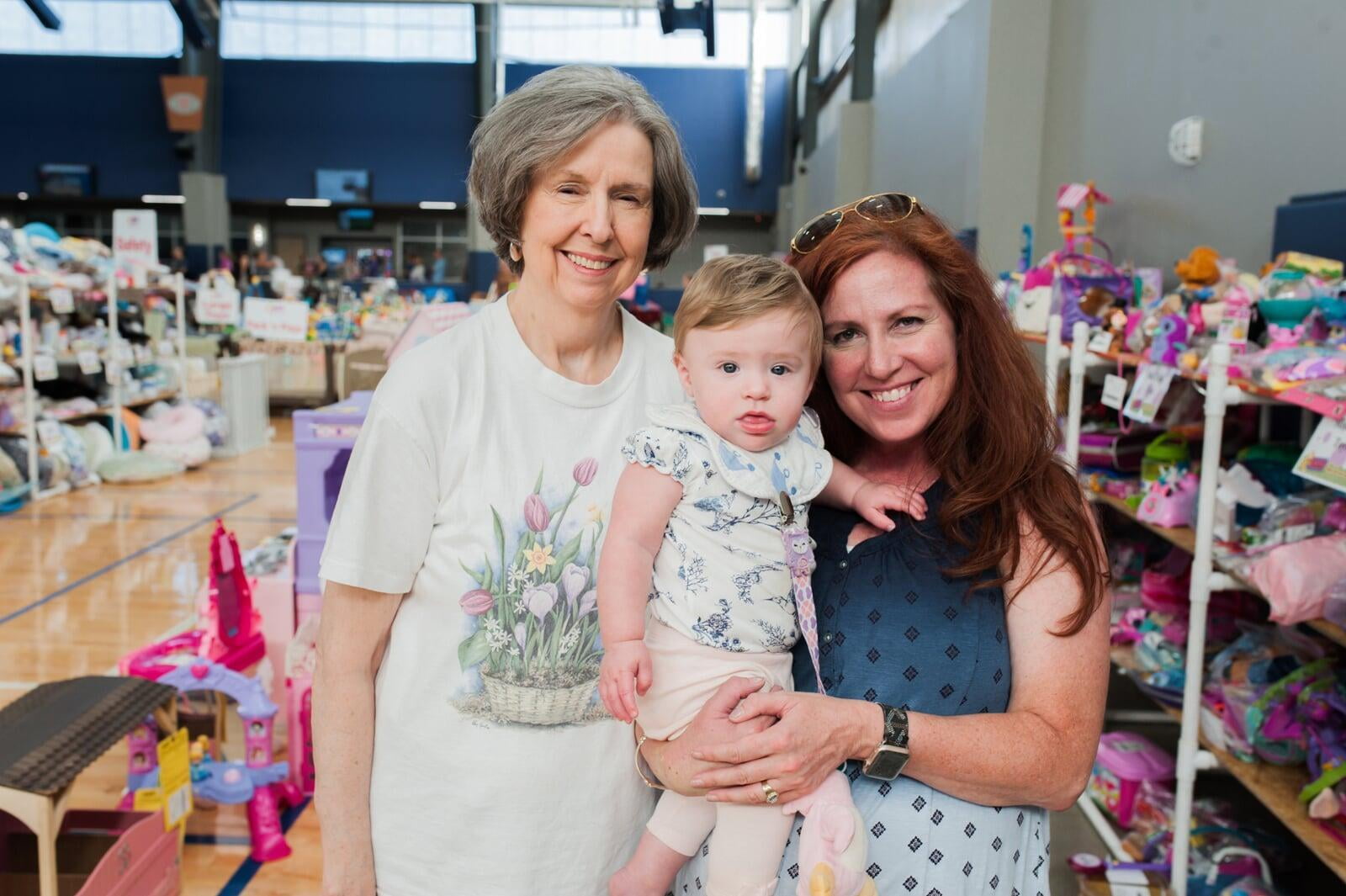 A young JBF shopper mom in a black Metallica T-shirt holds an outfit she intends to buy at her local JBF sale.